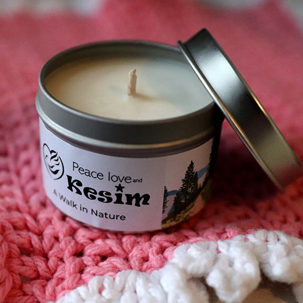 small white candle (unlit) in silver container. Lid is off and leaning on side of candle. Text on package reading "A Walk in Nature"