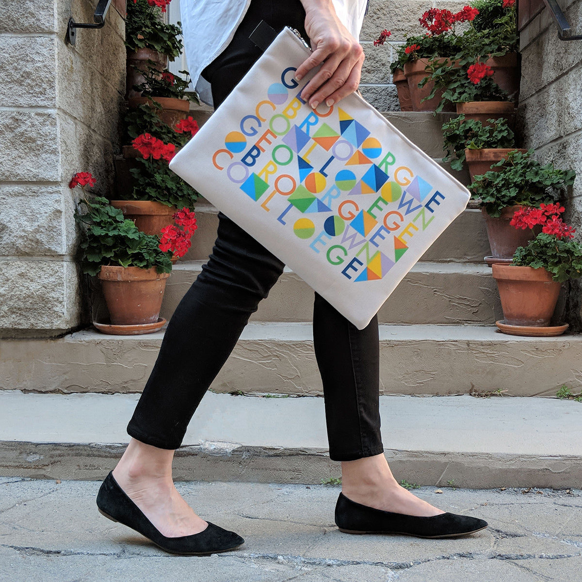 woman carrying large zip pouch featuring multicoloured george brown college text and geometric shape design