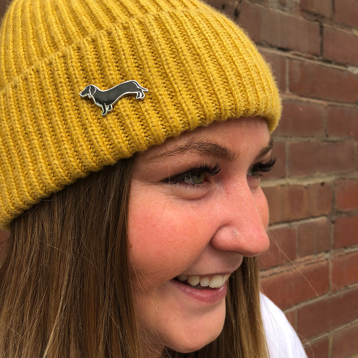 close up of a girl wearing a yellow beanie with black dachshund enamel pin on the front