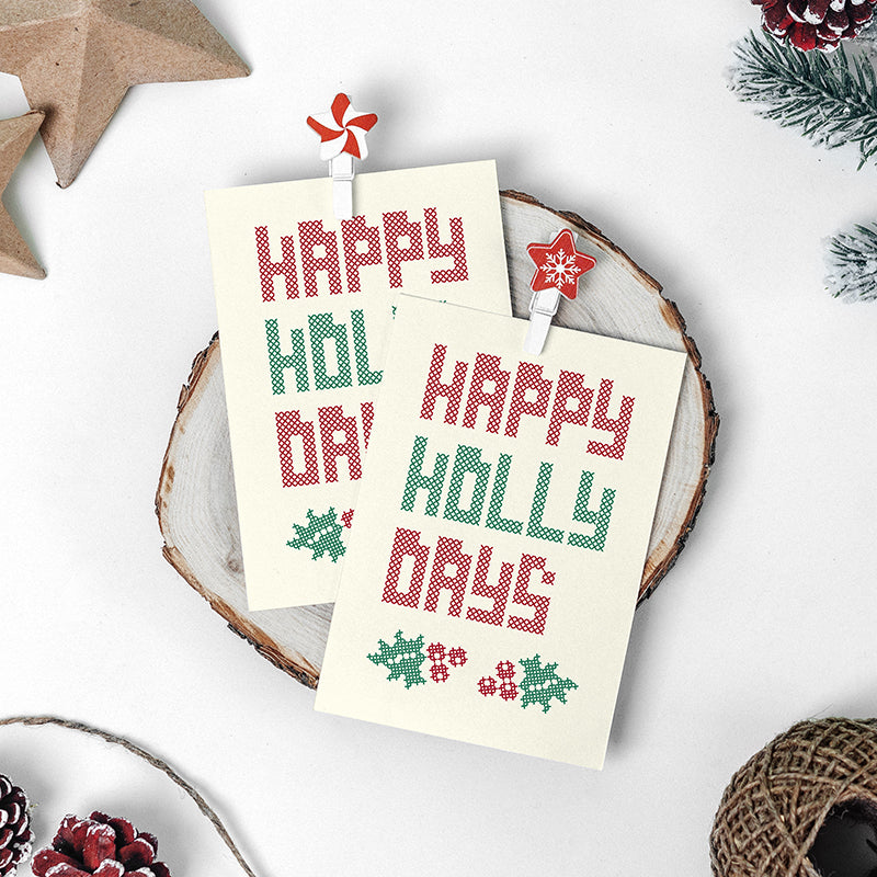 text reading 'happy holly days' and two holly icons in red and green on cream coloured card. Text and icons are made of small x's.