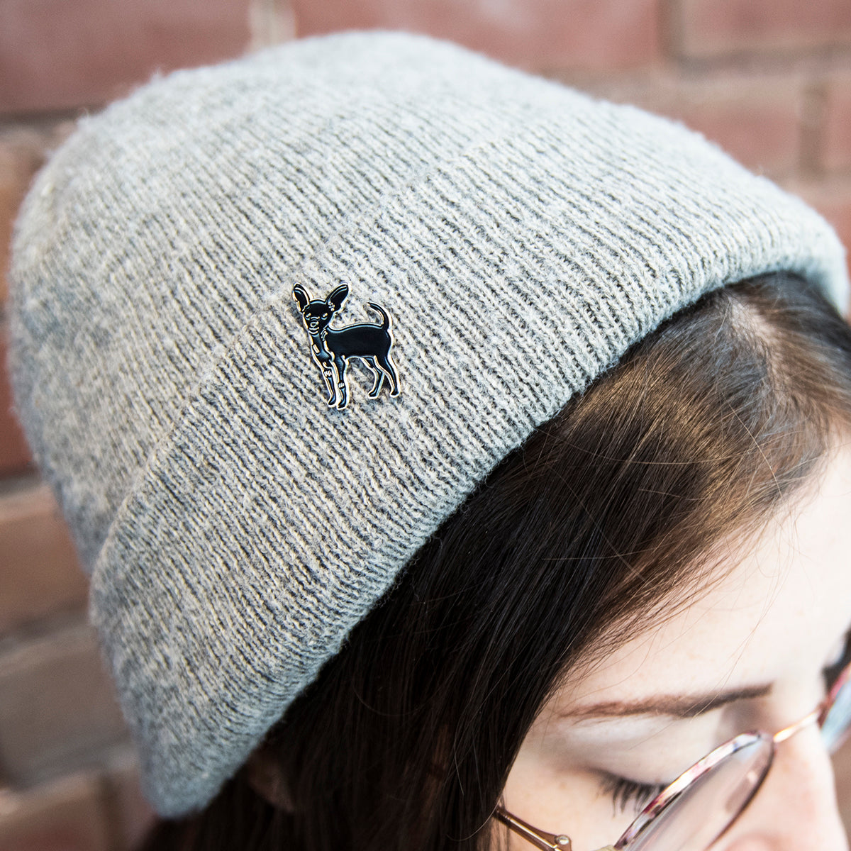 black chihuahua enamel pin featured on a grey beanie hat