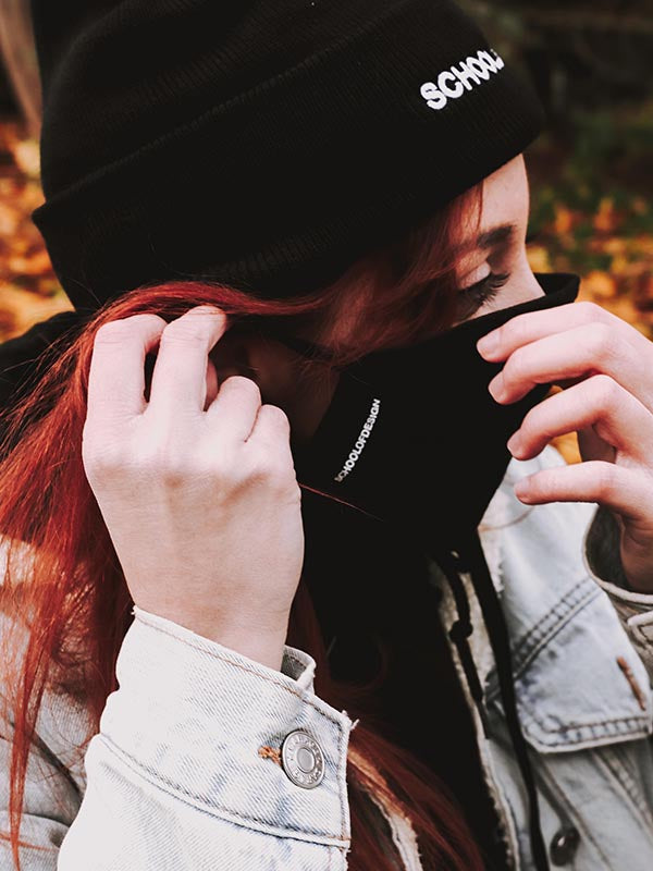 Person with red hair putting on black School of Design toque and black School of Design mask