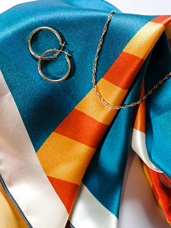 Silk bandana featuring lighthouse, sunset, and path through blue water. Shown with jewelry