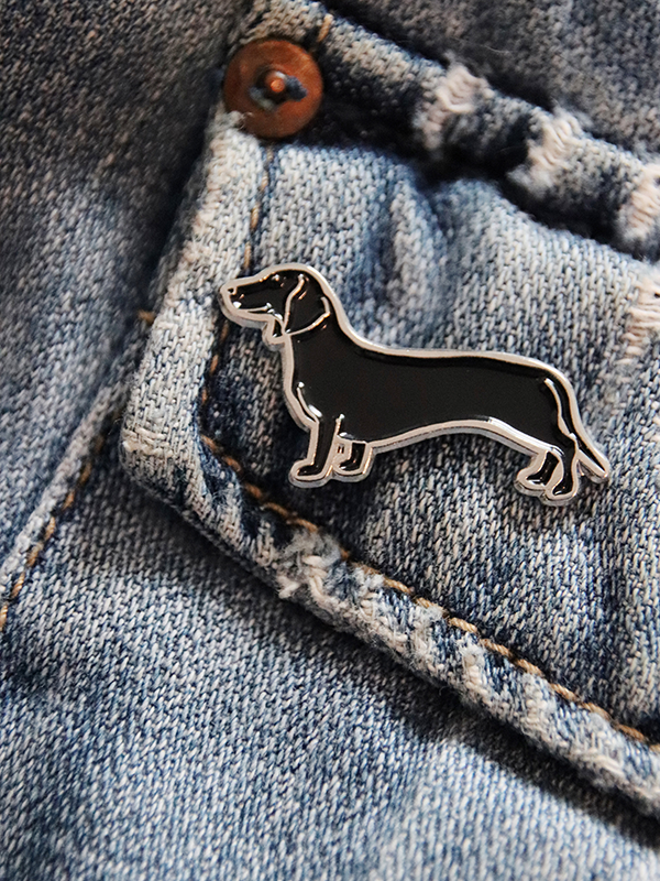 close up of black dachshund enamel pin pinned onto jean jacket