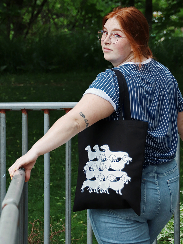 red haired girl wearing black tote bag with horizontal dog illustration pattern in white
