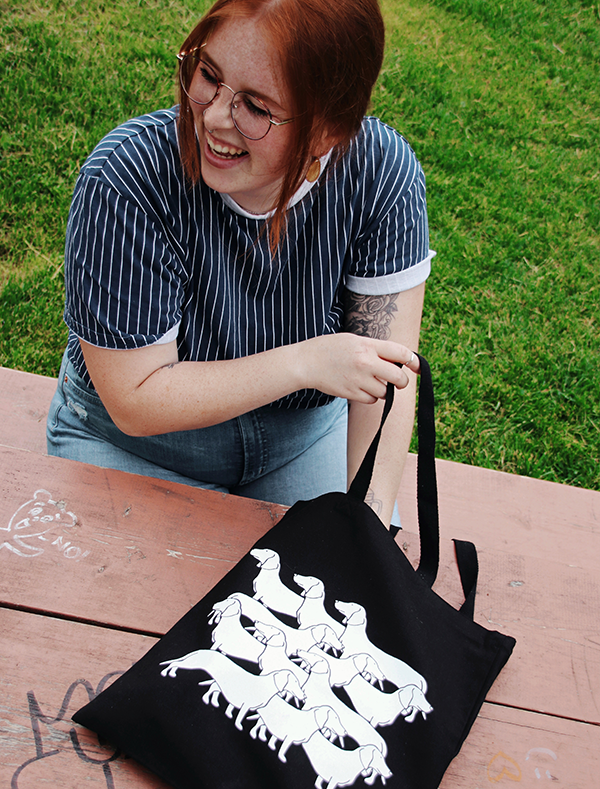 red haired girl smiling holding black tote bag with horizontal dog illustration pattern in white