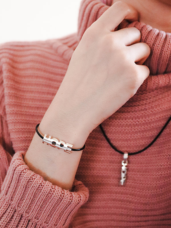 silver 'HOPE' bracelet and necklace worn by person in pink sweater