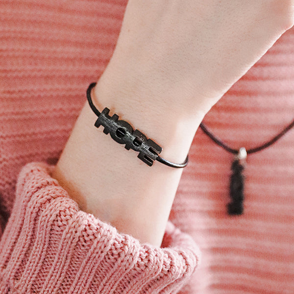 black 'hope' bracelet and necklace worn by person in pink sweater