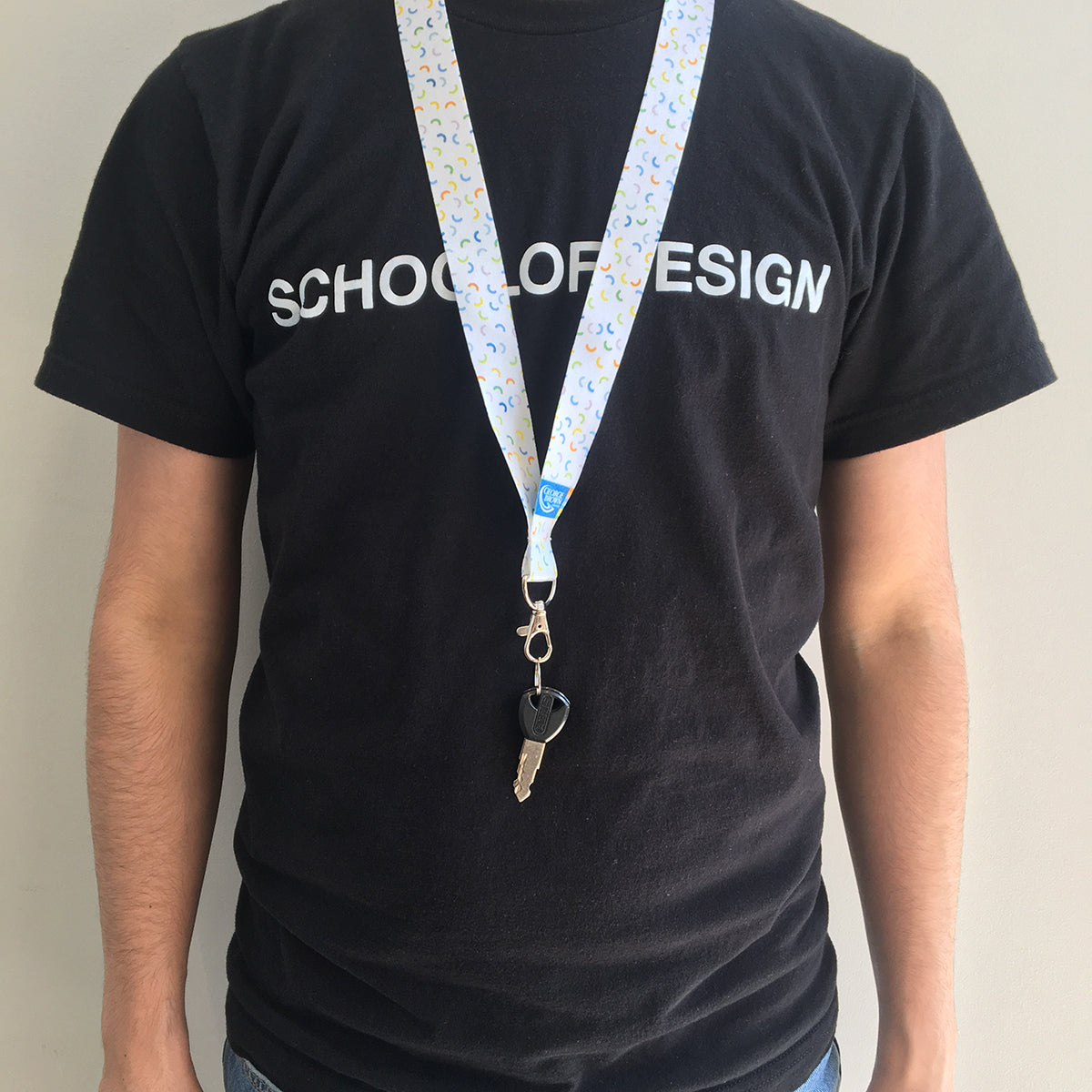 male wearing white lanyard with colourful macaroni pattern and school of design black cotton t shirt