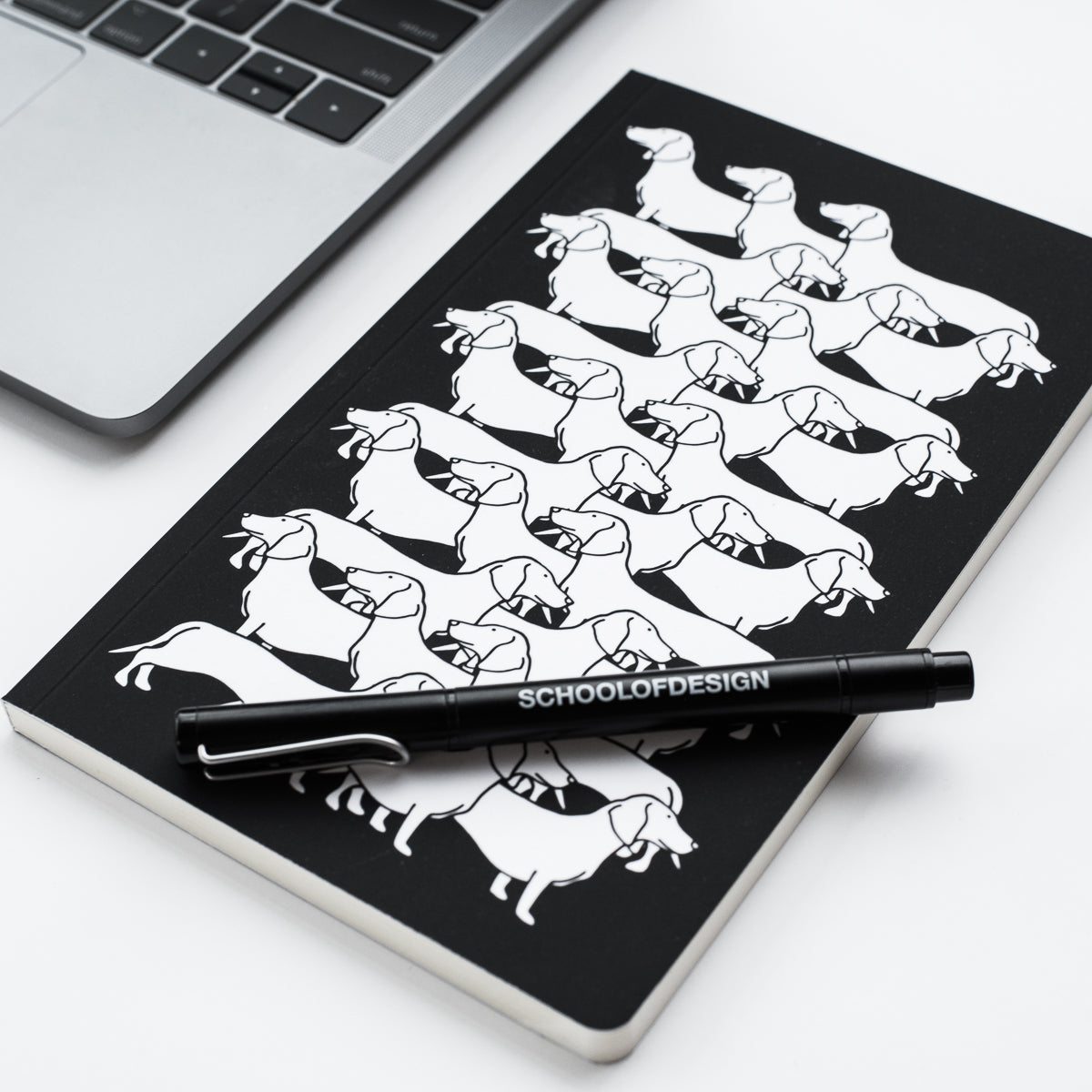 black notebook with horizontal dachshund illustration pattern in white, and black school of design pen