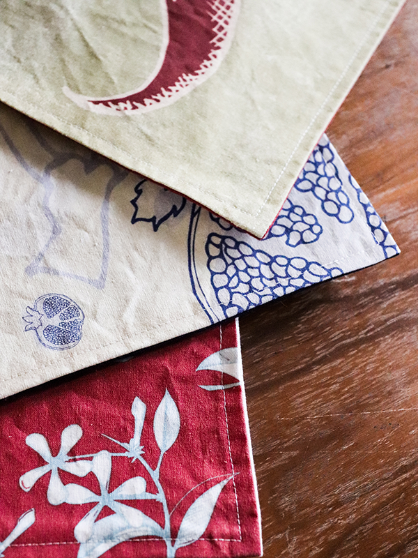 stack of assorted placemats; red pepper, blue fruit, and pomegranate placemats