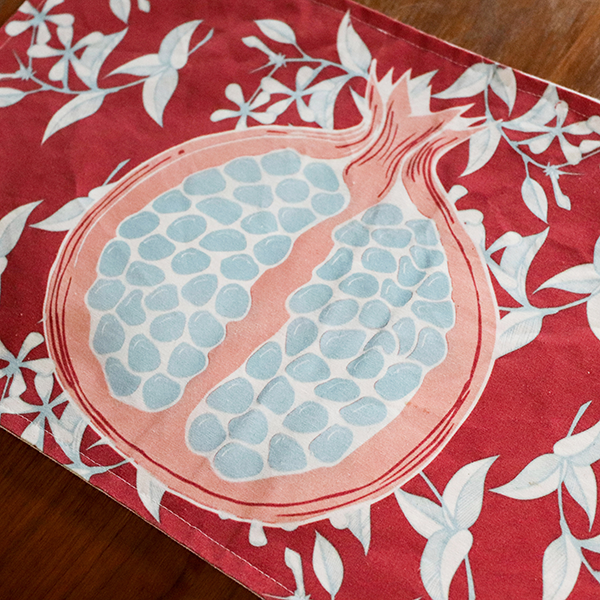13" x 20" 100% cotton canvas red placemat with student made pomegranate illustration in the middle, with floral and leave pattern in the background