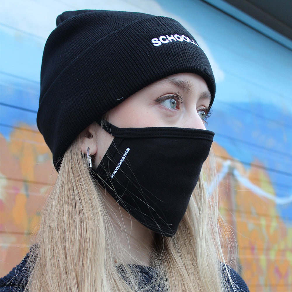 close up of blonde girl with black cotton non medical grade mask and black toque, both with school of design text in white