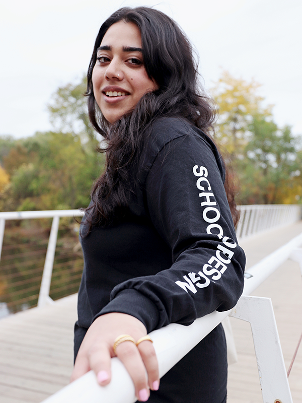 Person with long dark hair wearing a long sleeve with the words School of Design written down the arm.