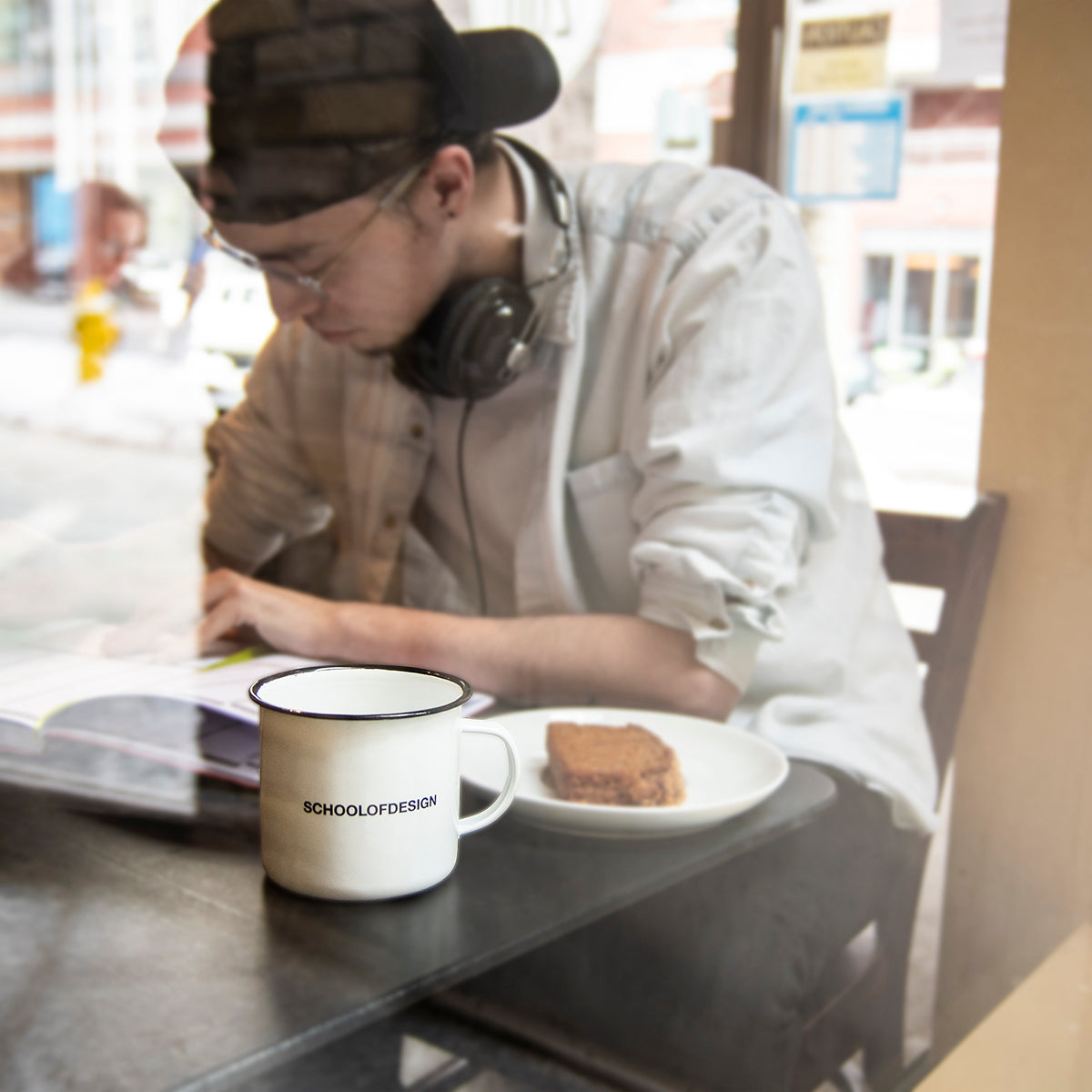 a student studying with white enamel mug featuring school of design text in black