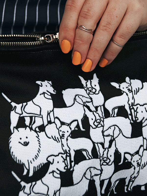 close up of a girls hand holding black zip case with mixed dog illustration in white